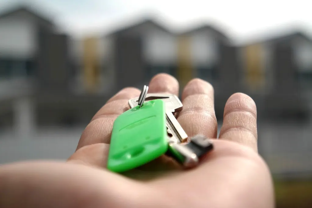 House keys in a hand in front of new homes